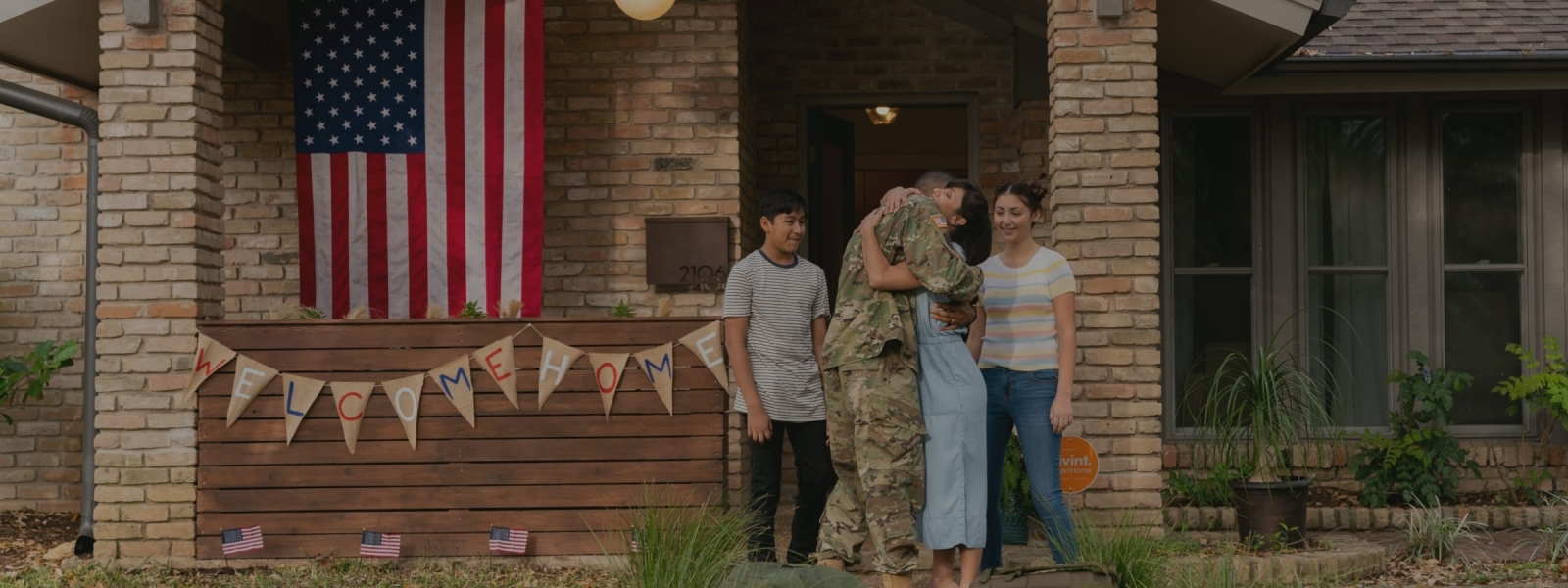 Service man hugging wife with kids on front porch