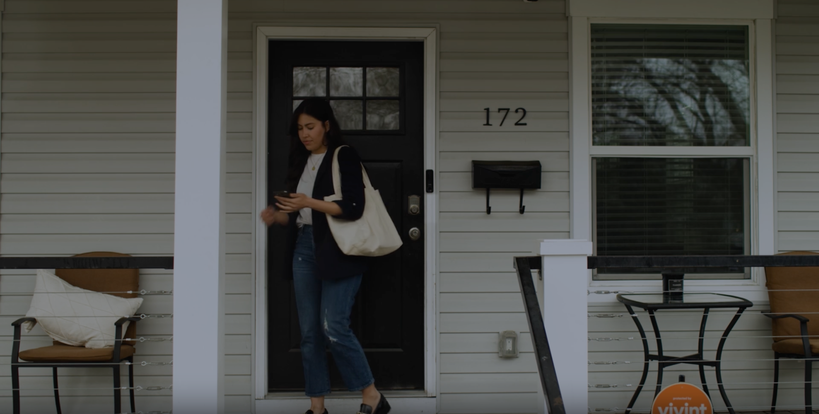 A woman checks her phone while closing her front door, which has a Vivint Doorbell Camera Pro mounted nearby