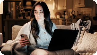 Woman sitting on couch looking at phone with open laptop