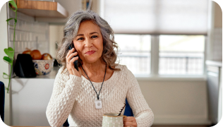 A Senior Woman wearing Senior Alert Device, smiling and speaking on the phone 