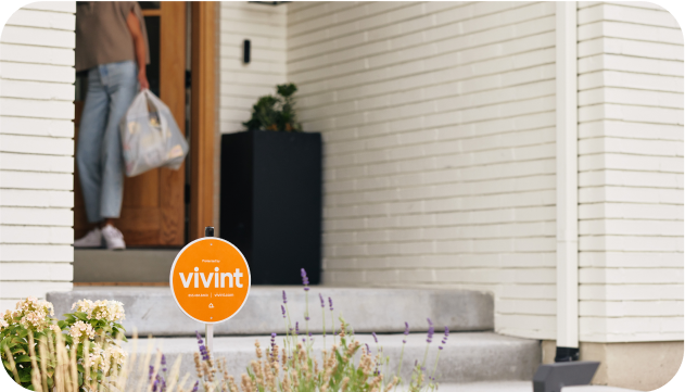 Person bringing groceries inside their home with a Vivint yard sign in yard