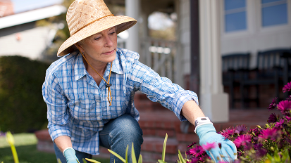 a woman planting flowers, wearing an emergency pendant on her wrist