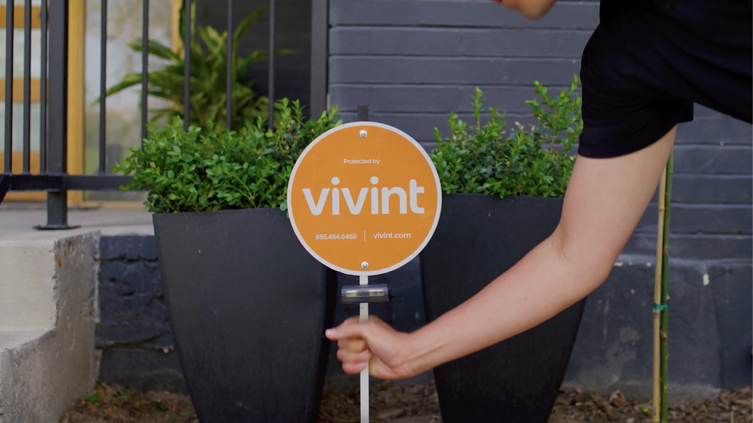 A hand holding a Vivint sign in front of a house