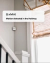 Vivint motion sensor on a wall next to a window, with a notification from the app saying "Motion detected in the hallway" hovered over