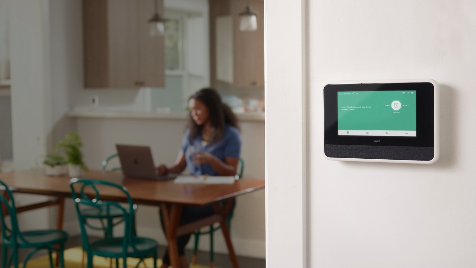View of Vivint Smart Hub installed on white wall and woman in the background with her laptop at the table