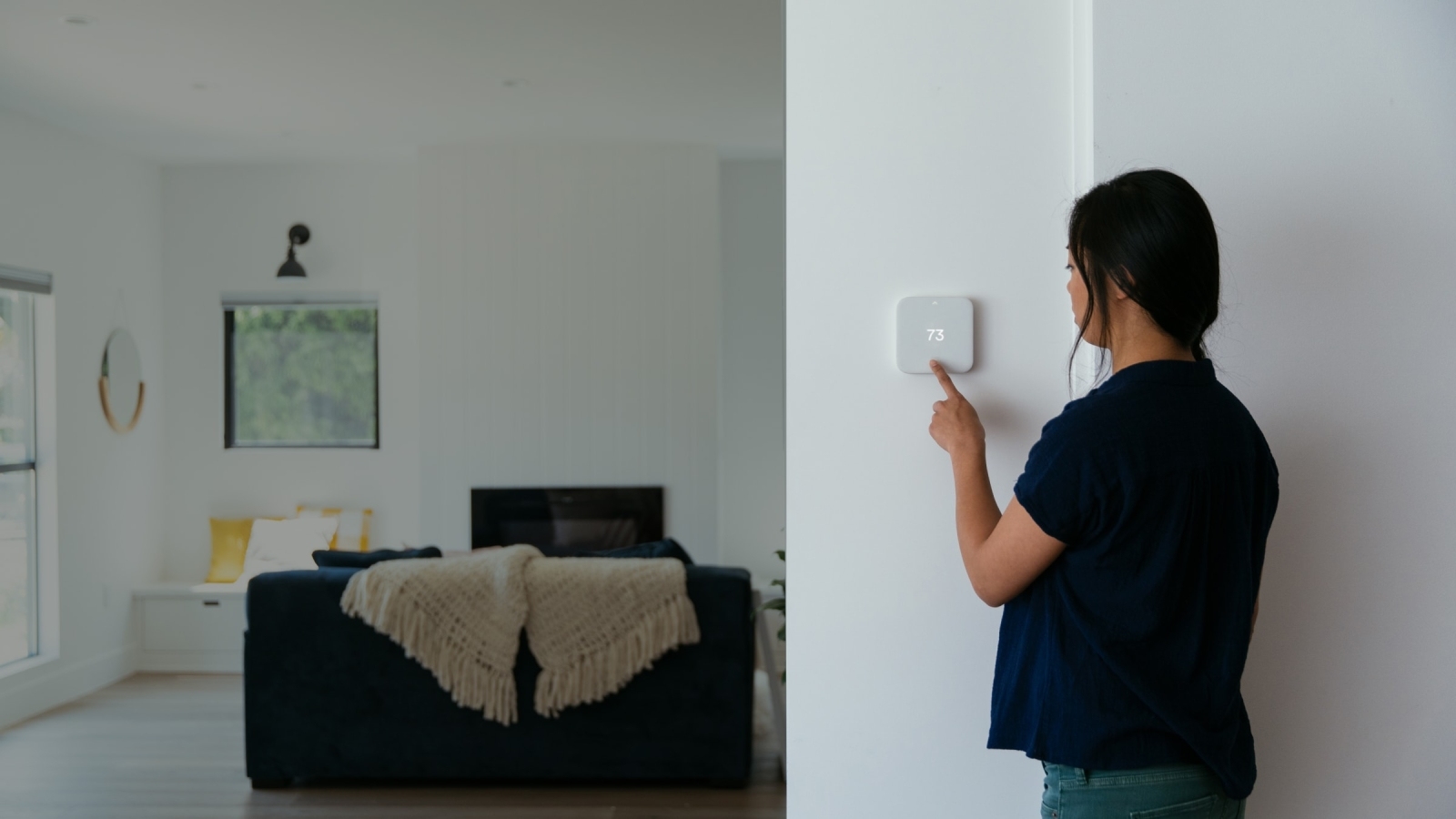 Women adjusting Vivint Smart Thermostat on white wall and view of living room
