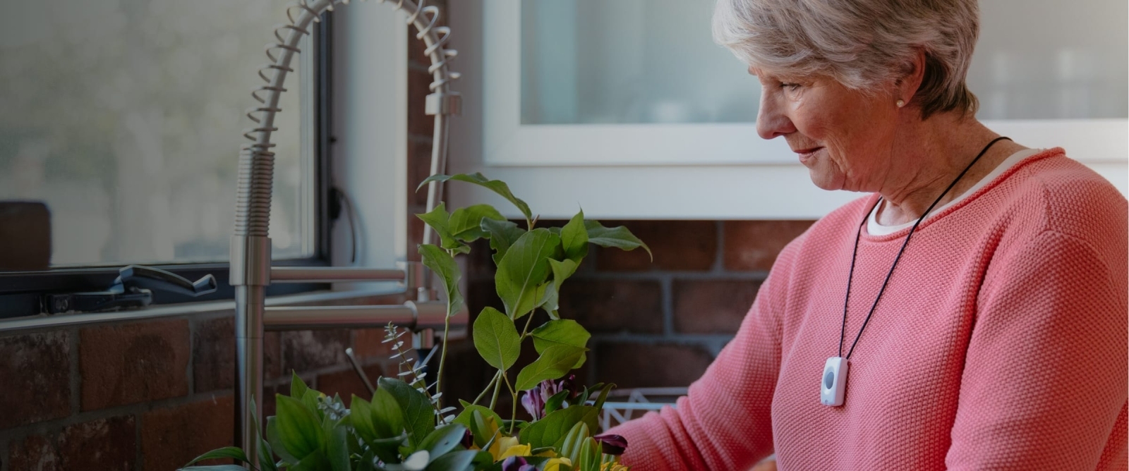 A woman wearing the emergency pendant necklace while taking care of a plant.