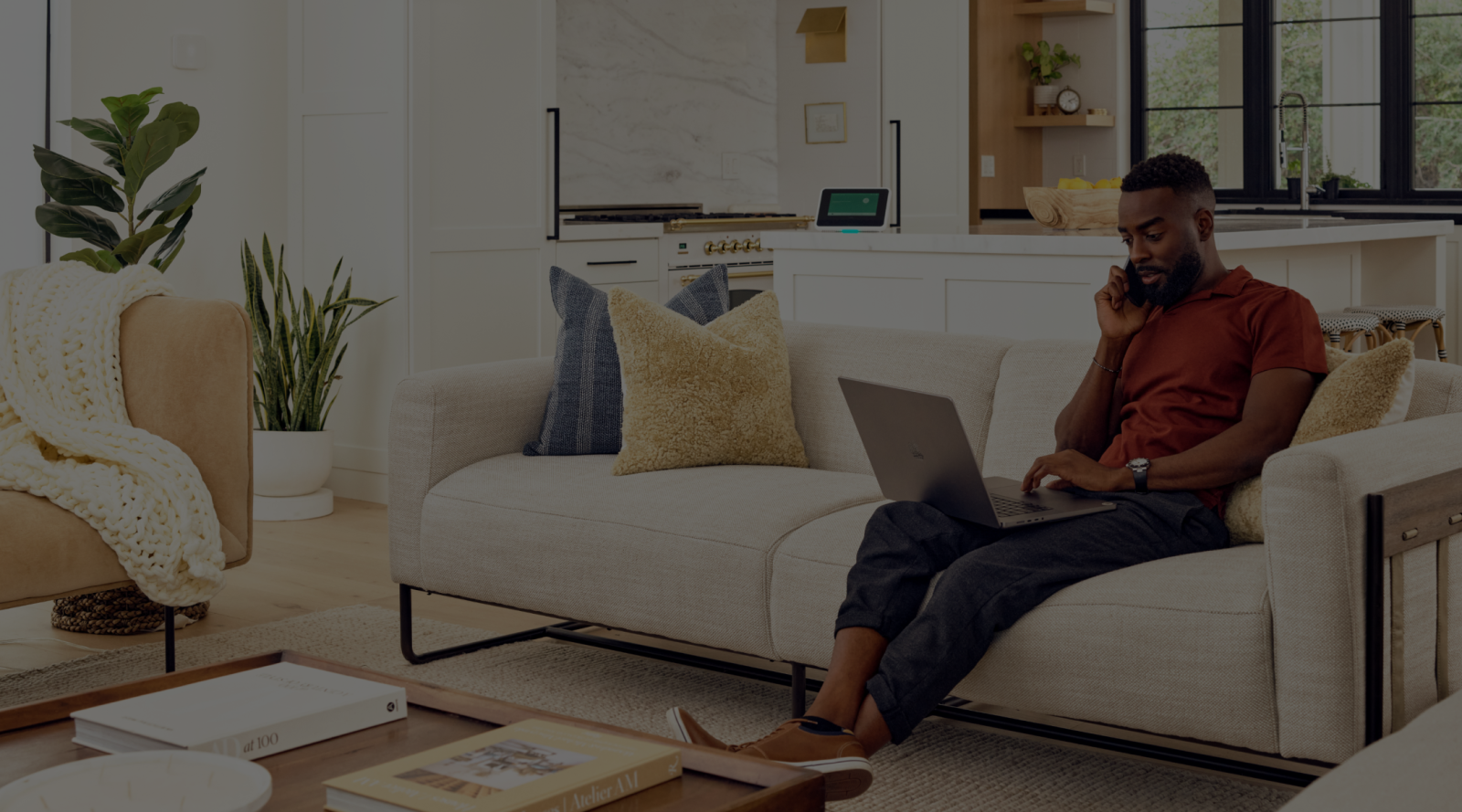 a man talking on his phone, sitting on the couch with a laptop on his lap.