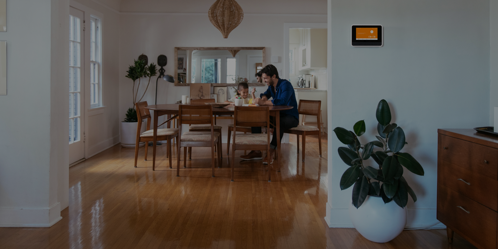 a father and daughter sitting at their dining table, laughing, next to Vivint smart hub on the wall in the kitchen