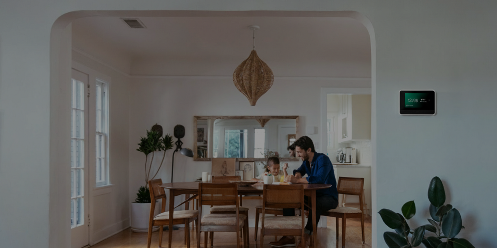 a father and daughter sitting at their dining table, laughing, next to Vivint smart hub on the wall in the kitchen