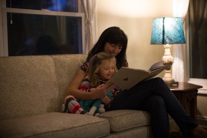 Mother and daughter reading a book on the couch.