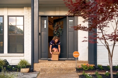 Woman opening her front door to pick up a package on her porch.