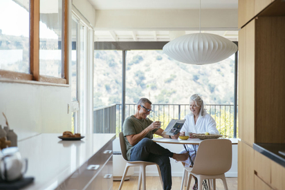 Older couple sitting at the table reading the newspaper.
