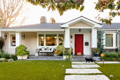Modern suburban home with white exterior, red front door, landscaped yard, and visible smart home security sign