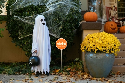 Child dressed as a ghost next to a Vivint sign.