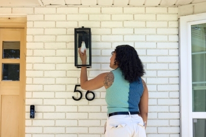 Woman installing a smart light bulb on her front porch.