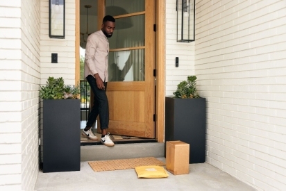A man opening his front door to grab packages from his front porch.