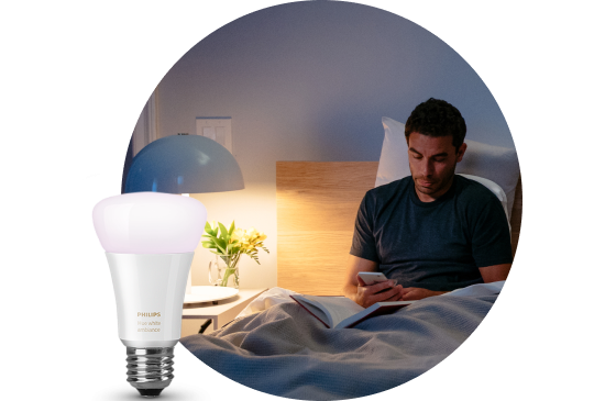 Image with a smart light bulb in the forefront with a lit nightstand lamp in the background