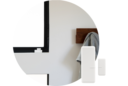 Security Sensors in the forefront with a coat hanger installed on a white wall holding a grey coat
