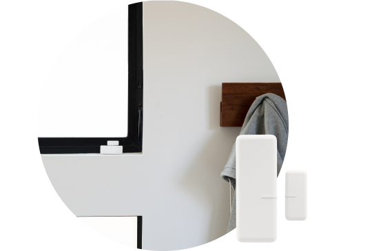 Security Sensors in the forefront with a coat hanger installed on a white wall holding a grey coat