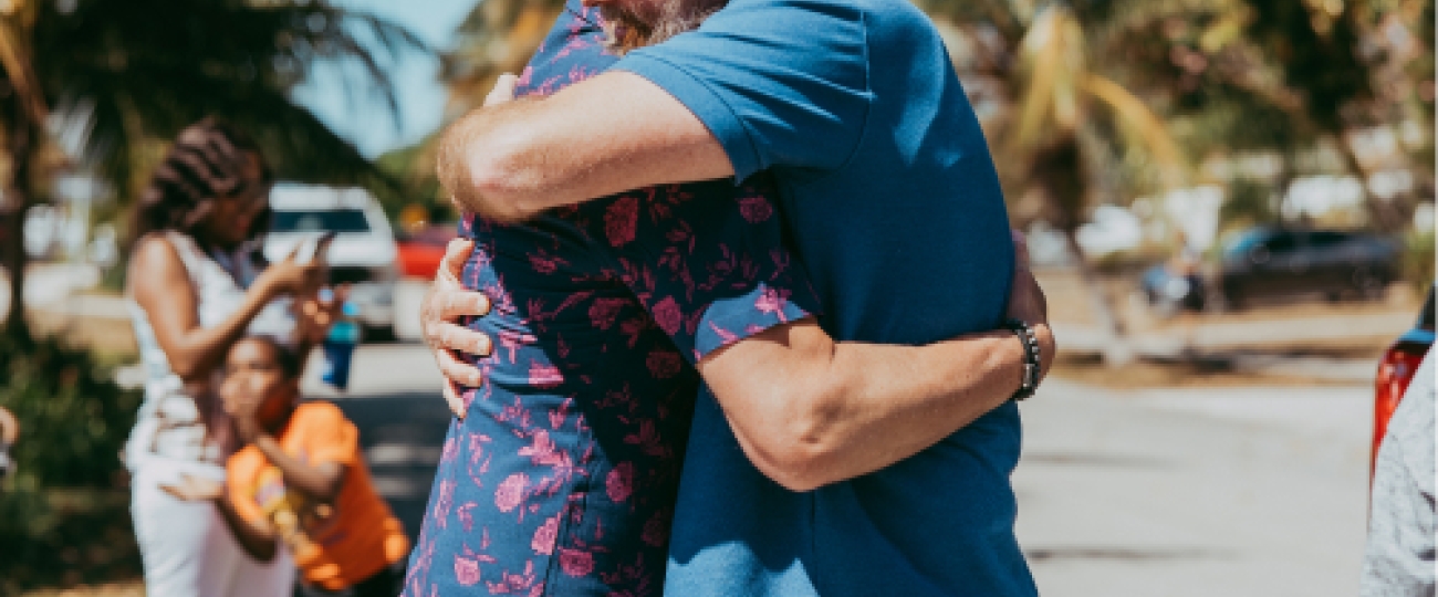 Two people hug with palm trees in the background